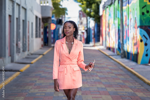 Young woman wearing a blazer dress walking on a paved brick street in Downtown Kingston, Jamaica