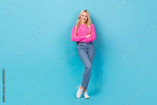 Portrait of satisfied pleasant woman curly hairstyle wear knit pullover denim pants standing arms folded isolated on blue color background
