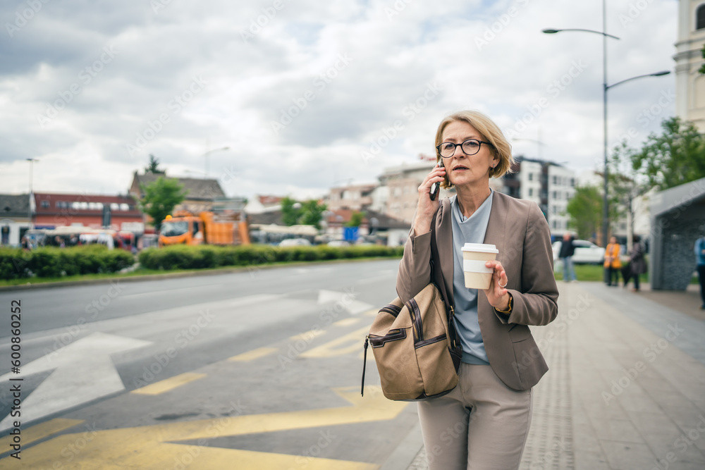 Fototapeta premium mature woman stand at city bus stop use smartphone while wait drive