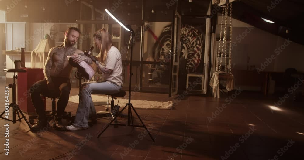 Female tattooist making tattoo to shirtless male customer in salon Female tattooist making tattoo to shirtless male customer in salon