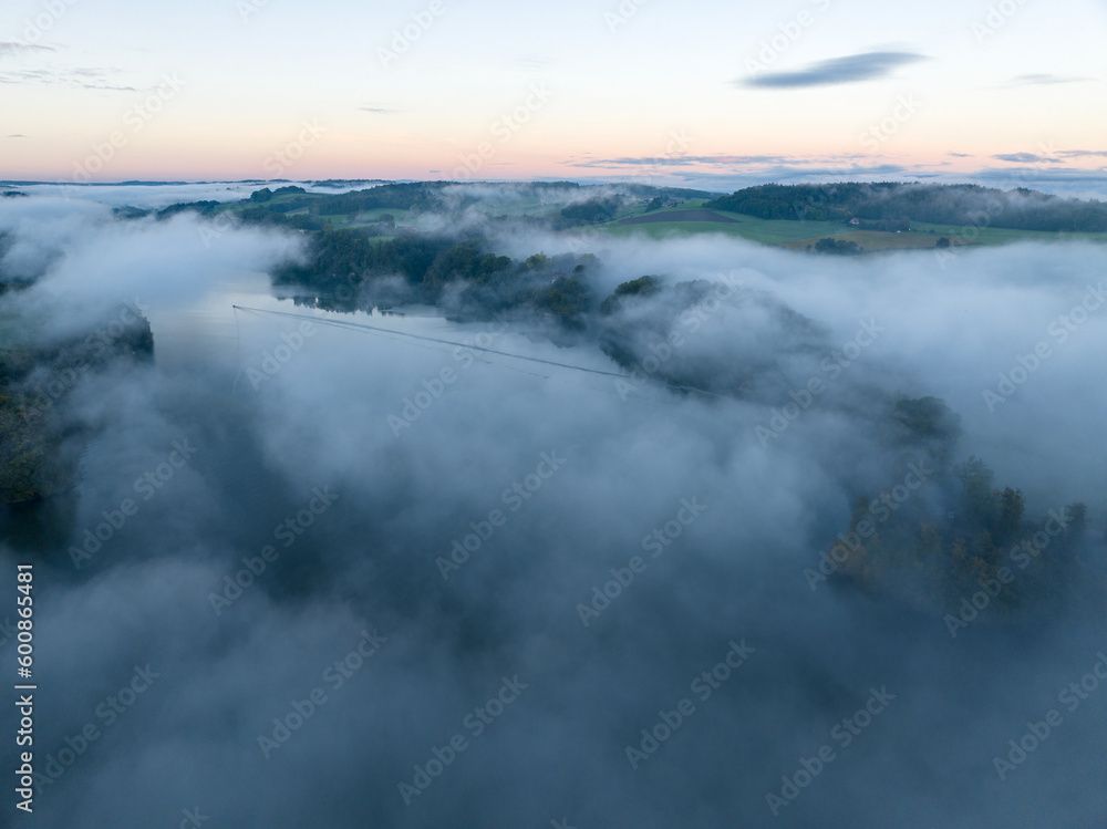 Aerial view of fog above lake early in the morning during sunrise. Misty scenery with reflections.