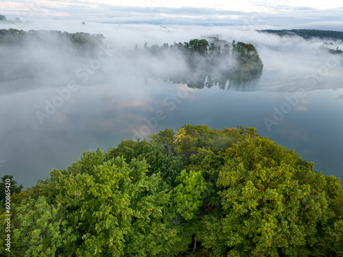 Aerial view of fog above lake early in the morning during sunrise. Misty scenery with reflections. © Mario