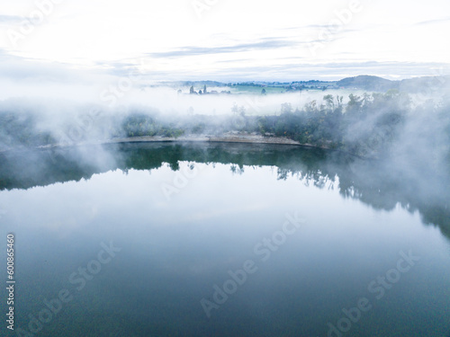 Aerial view of fog above lake early in the morning during sunrise. Misty scenery with reflections.