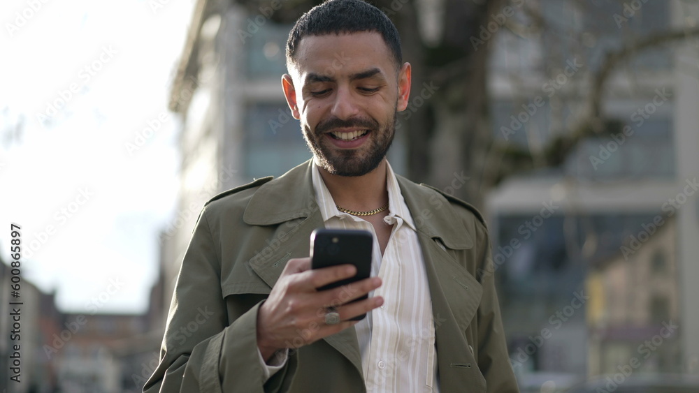 One happy Moroccan man smiling at social media content online while holding smartphone device standing in city street. Closeup face of a Middle Eastern man in tracking shot with motion One happy Moroccan man smiling at social media content online while holding smartphone device standing in city street. Closeup face of a Middle Eastern man in tracking shot with motion