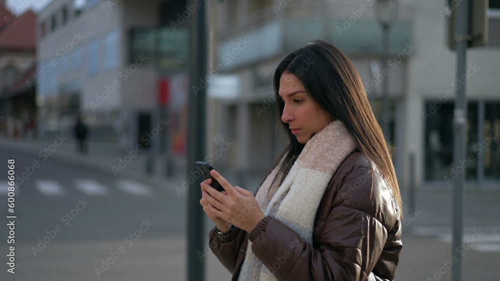 One Young Woman looking at cellphone device standing in city street. Tracking moving shot of adult girl in 20s staring at screen