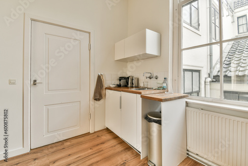 a kitchen area with wood flooring and white cupboards, an open window is in the corner to the room