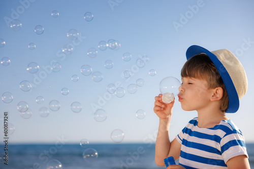 Kid having fun on the beach. Boy blowing soap bubbles