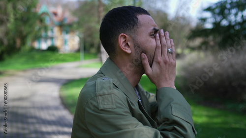 Troubled man covering face in shame and anxiety. A Desperate depressed Middle Eastern person stands outdoors at park feeling worry and preoccupation