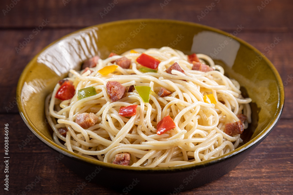 Plate with spaghetti, bacon and chopped vegetables.