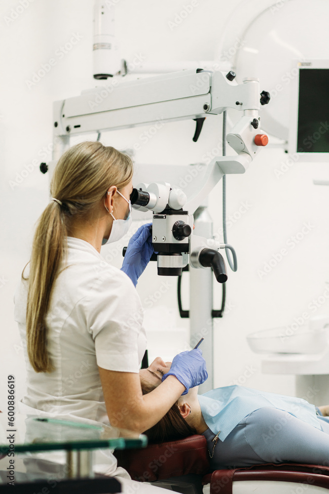 Fototapeta premium Female dentist using dental microscope treating patient teeth at dental clinic office.