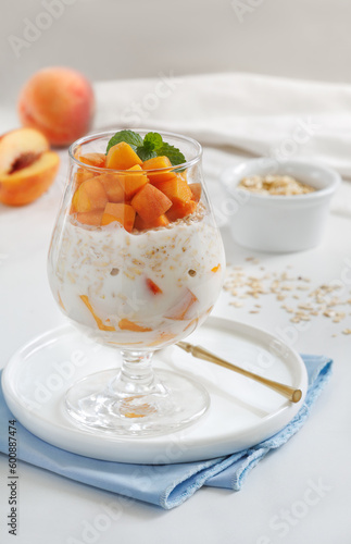 Peaches and Cream Overnight Oats. Healthy breakfast made with oats soaked for the night in milk or yogurt layered with cubes of fresh peaches, served in a clear glass. Selective focus, vertical.