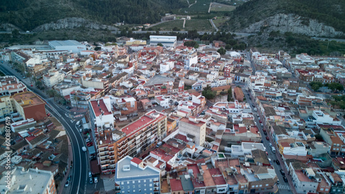 Aerial view of a Spanish city with bustling structures and a blue building at the center. Vineyard and mountains in the distance.