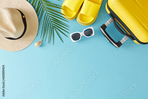 Embrace the beauty of the season with our summer travel concept. Top view flat lay of trendy yellow suitcase beach accessories and palm leaf on light blue background with space for text
