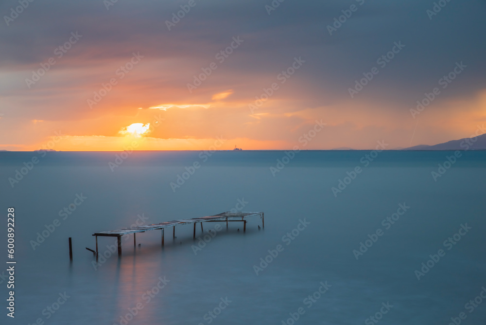 Wooden pier built into the sea and helping fishing, sunset colors and light