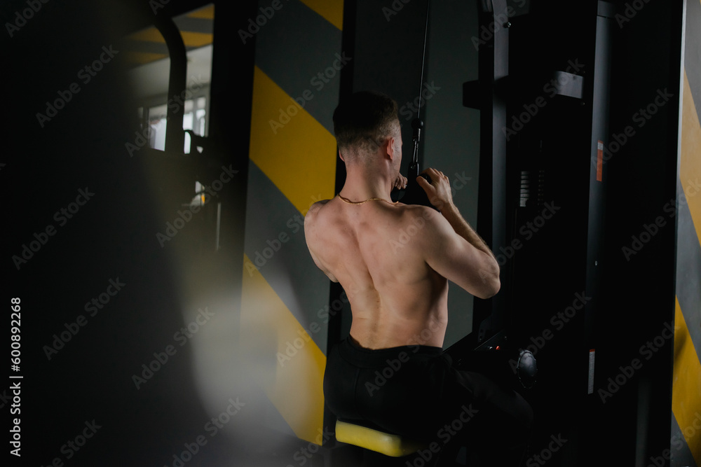 A strong male bodybuilder shakes his biceps in the gym with a barbell and dumbbells, at this time the muscles are tense A strong male bodybuilder shakes his biceps in the gym with a barbell and dumbbells, at this time the muscles are tense