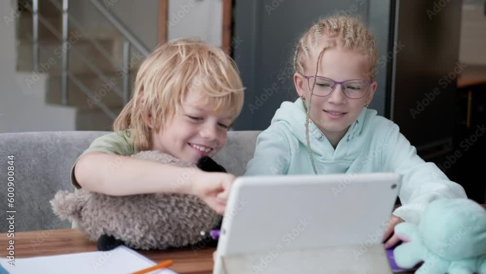 Online school class, siblings pupils boy and girl learning together remotely online at home, looking to digital tablet, speaking with teacher or tutor using internet Online school class, siblings pupils boy and girl learning together remotely online at home, looking to digital tablet, speaking with teacher or tutor using internet