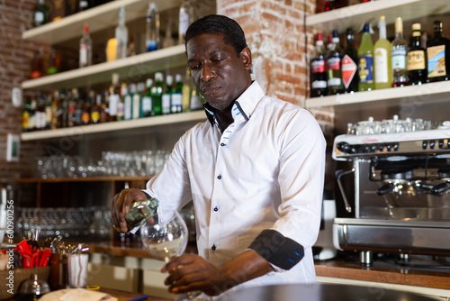Portrait of an experienced African bartender pouring a drink into a glass at his workplace