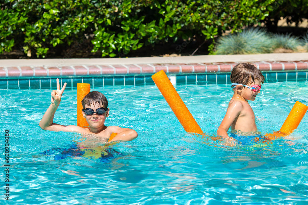 Oudoor summer activity. Concept of fun, health and vacation. Happy smiling boys eight and five years old in swim glasses swiming in the pool with noodles on hot summer day.
