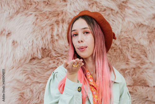 Stylish millennial teenager girl with color hair sends an air kiss. Portrait of a romantic young woman in a beret on a pink background. photo