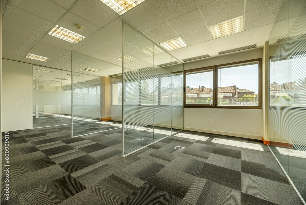 Empty offices with several glass partitions separating cubicles, long windows Empty offices with several glass partitions separating cubicles, long windows