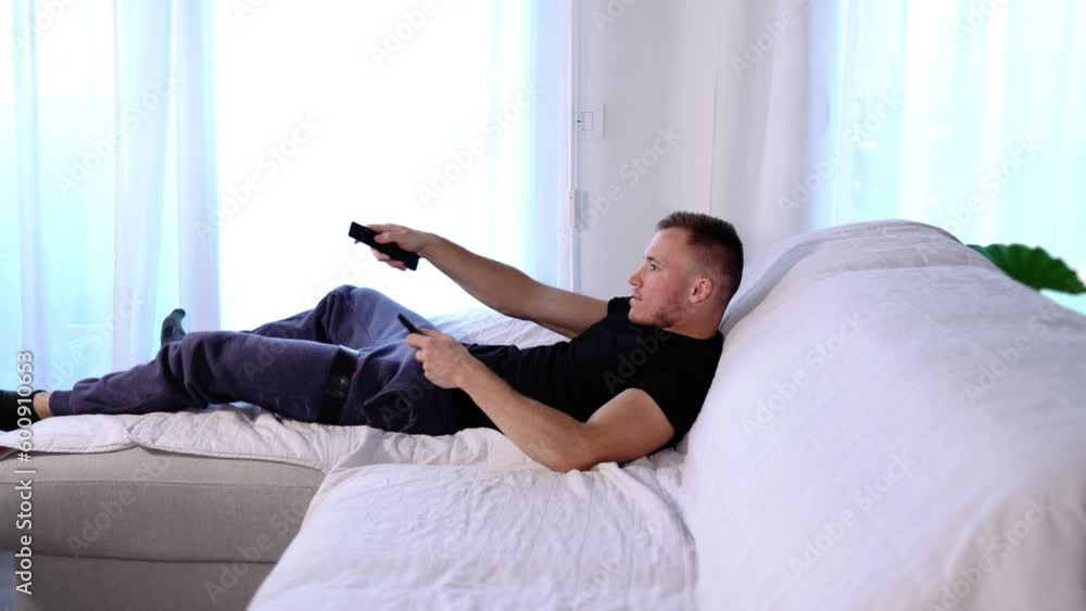 Muscular guy jumps on sofa presses remote controller buttons Muscular guy jumps on sofa presses remote controller buttons