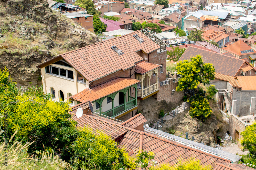 House, residential building with red tiled roof and carved wooden balconies on mountain cliff in old historic city town Tbilisi, Georgia top view. Scenic summer landscape House, residential building with red tiled roof and carved wooden balconies on mountain cliff in old historic city town Tbilisi, Georgia top view. Scenic summer landscape