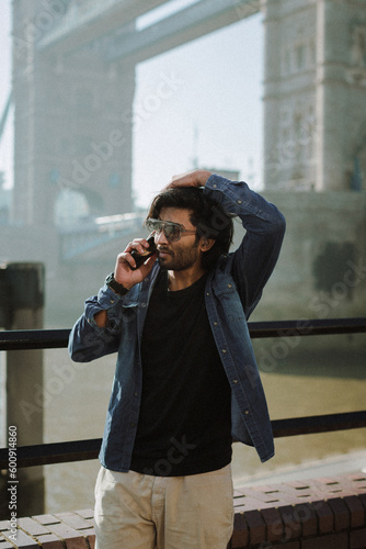 Quadro em tela Handsome stylish guy from India calling by phone near the Tower Bridge London