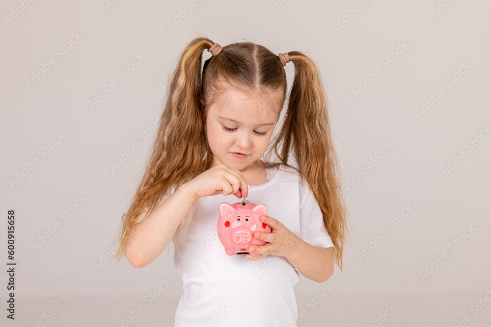 Positive girl in casual outfit laughing and saving money in piggy bank against white background Positive girl in casual outfit laughing and saving money in piggy bank against white background