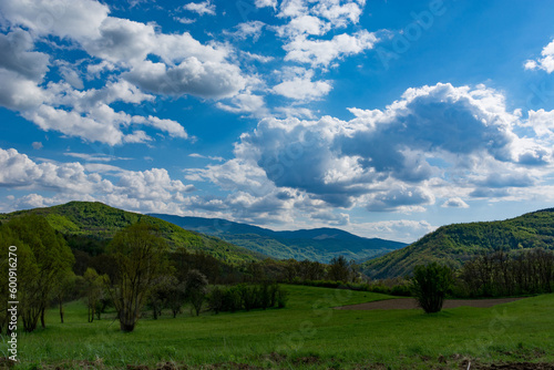 A landscape of nature with sunlit hills and meadows, accompanied by white fluffy clouds in the sky on a sunny spring day