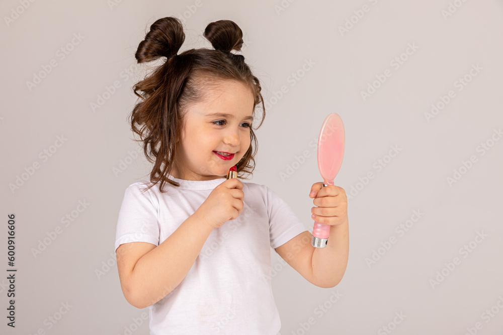 Happy little girl puts lipstick on her lips looking in the mirror at home. Little trendy. little girl applying makeup Happy little girl puts lipstick on her lips looking in the mirror at home. Little trendy. little girl applying makeup