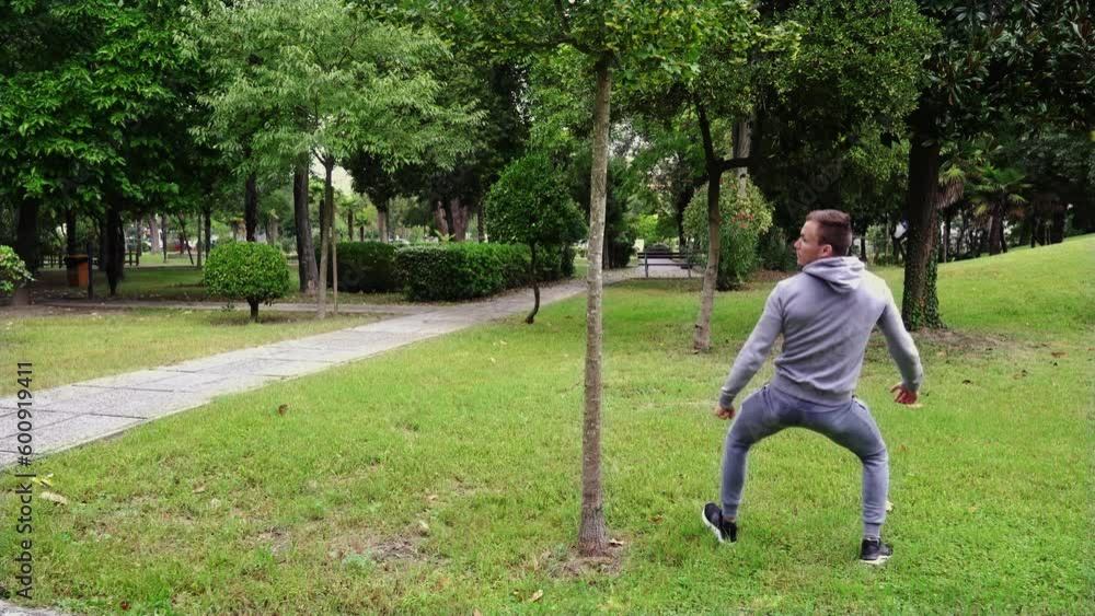 Young man plays fool hiding and looking out of young tree Young man plays fool hiding and looking out of young tree