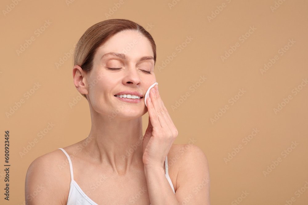Beautiful woman removing makeup with cotton pad on beige background, space for text Beautiful woman removing makeup with cotton pad on beige background, space for text