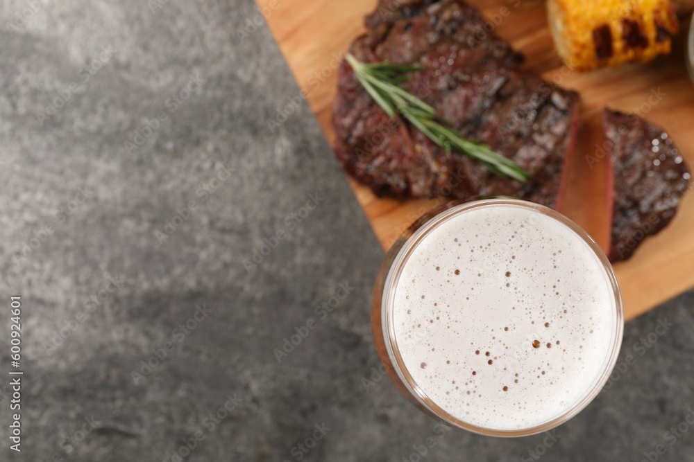Glass of beer, delicious fried steak and corn on grey table, flat lay. Space for text Glass of beer, delicious fried steak and corn on grey table, flat lay. Space for text