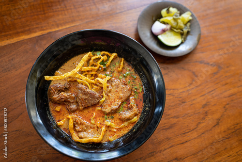 Khao Soi or Kao Soi Thai Curry Soup Noodles with braised beef and Thai spicy egg noodles on a wooden table. The delicious favorite famous Thai Food.