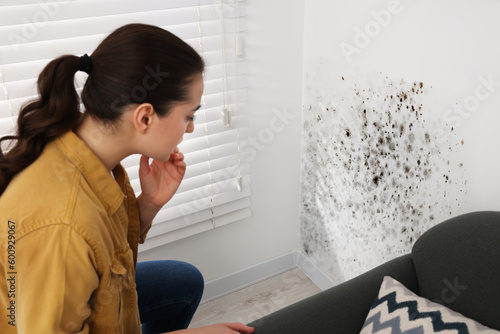 Woman looking at affected with mold walls in room photo