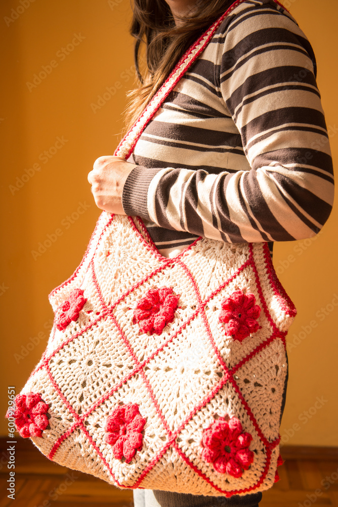 Young woman posing with a crocheted tote bag, with red flowers