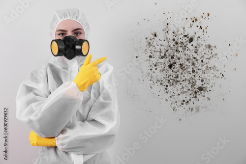 Woman in protective suit pointing at wall affected with mold