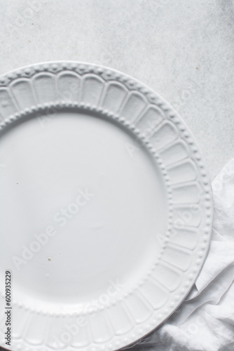 Top view of a large white ceramic plate with scalloped edges, a round white ceramic dinner plate on a marble surface 