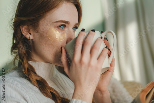 Fototapeta Naklejka Na Ścianę i Meble -  Close-up portrait of a young woman with beautiful blue eyes having a coffee in the morning in bed. People lifestyle portrait. Woman relaxing in her living room