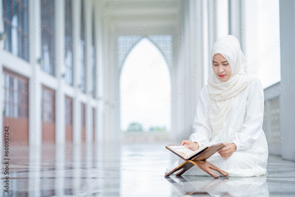 Obraz premium The image of an Asian Muslim woman in the Islamic religion in hijab in white color. reading the Quran and having a happy smiling face Staying in a beautiful mosque out of respect for God.