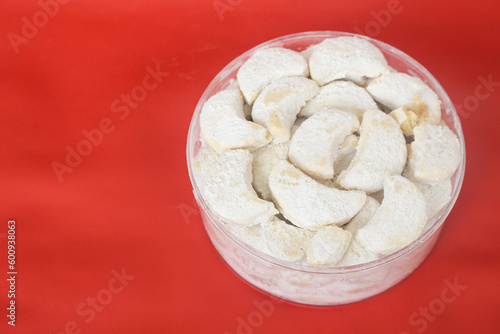 Kue putri salju or princess snow cookies. Is melt in the mouth cookies has a shape of crescent coated in icing sugar and popular indonesian cookies for Eid Mubarak. In red background.