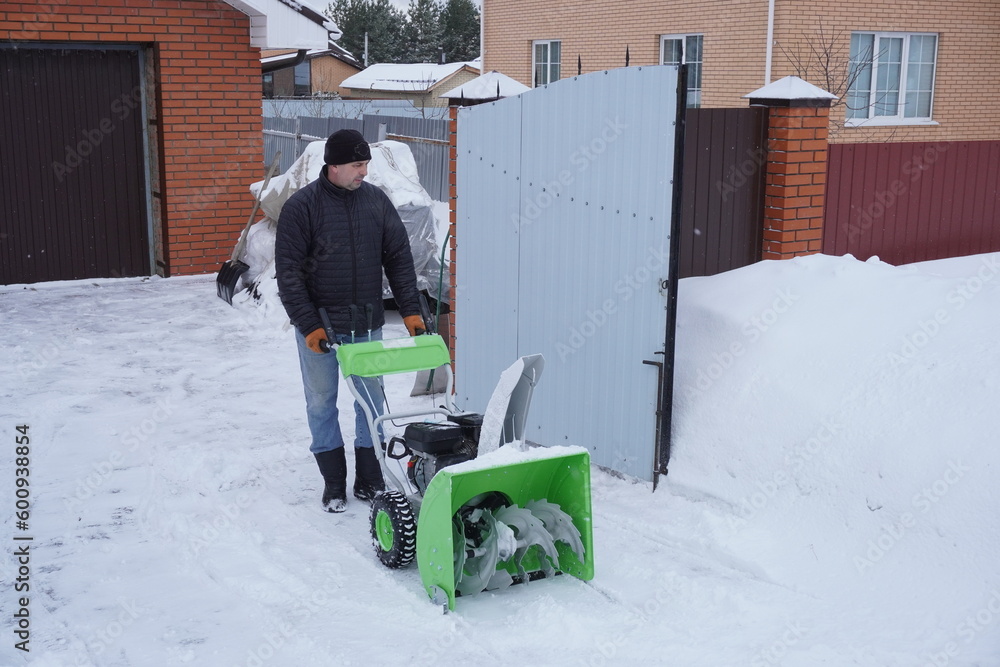 A man cleans snow in the winter in the courtyard of the house, man cleaning snow with a snow blower A man cleans snow in the winter in the courtyard of the house, man cleaning snow with a snow blower
