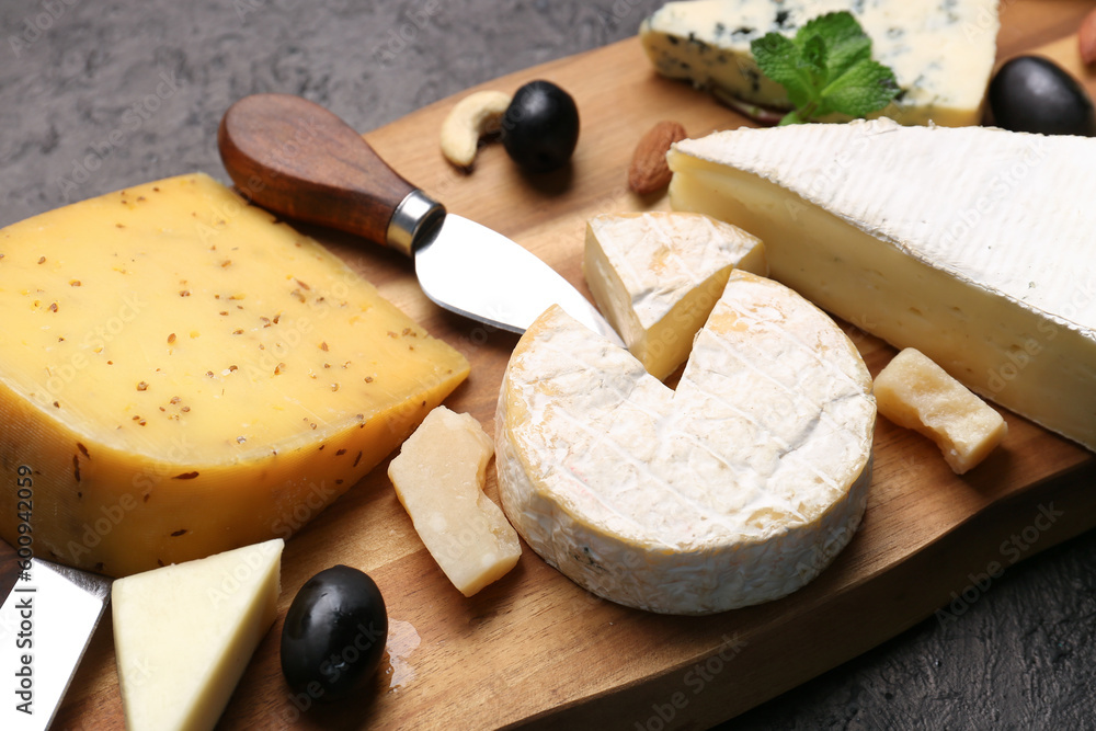 Wooden board with different types of tasty cheese on dark background, closeup