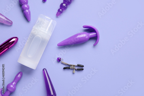 Bottle of lubricant and sex toys on lilac background