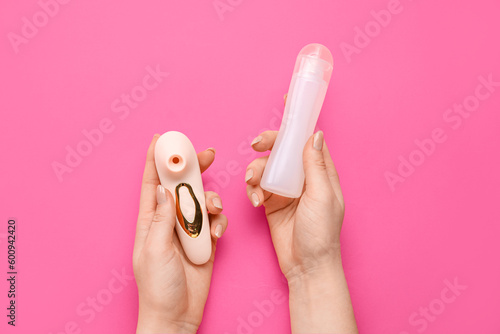 Woman holding vibrator and bottle of lubricant on pink background