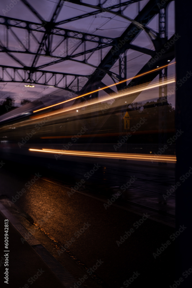 Naklejka premium Defocused Lights of cars at night in Krakow bridge. Street line lights. Night highway city. Long exposure photograph night road. Colored bands of red light trails on the road. Background wallpaper