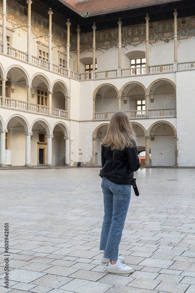 Female traveler in historical places looks around courtyard of landmark in Krakow Wawel castle. Tourist in historic place on sunny day. woman Tourism and blogging sharing live online for audience