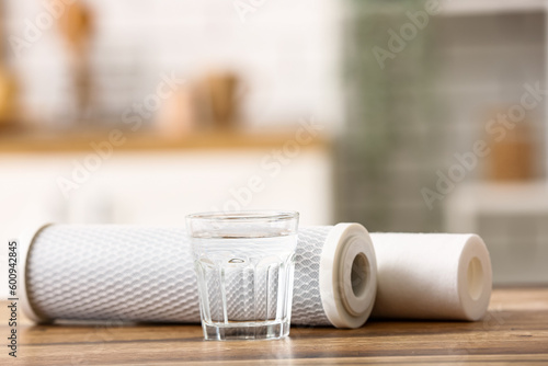 Glass of water with filters on wooden table in kitchen