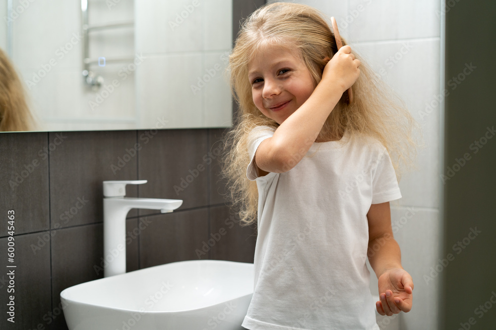 little blonde girl combing hair in the bathroom, caring for a child's hair little blonde girl combing hair in the bathroom, caring for a child's hair