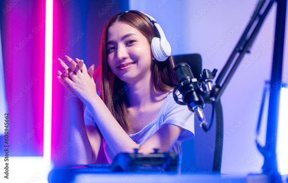 Professional gamer. Young asian pretty woman sitting on chair with computer pc in living room. Happy female Professional Streamer chinese wearing headphone playing game online in dark room neon light Professional gamer. Young asian pretty woman sitting on chair with computer pc in living room. Happy female Professional Streamer chinese wearing headphone playing game online in dark room neon light